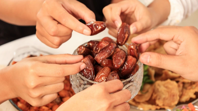 Multiple hands picking dates from a bowl.