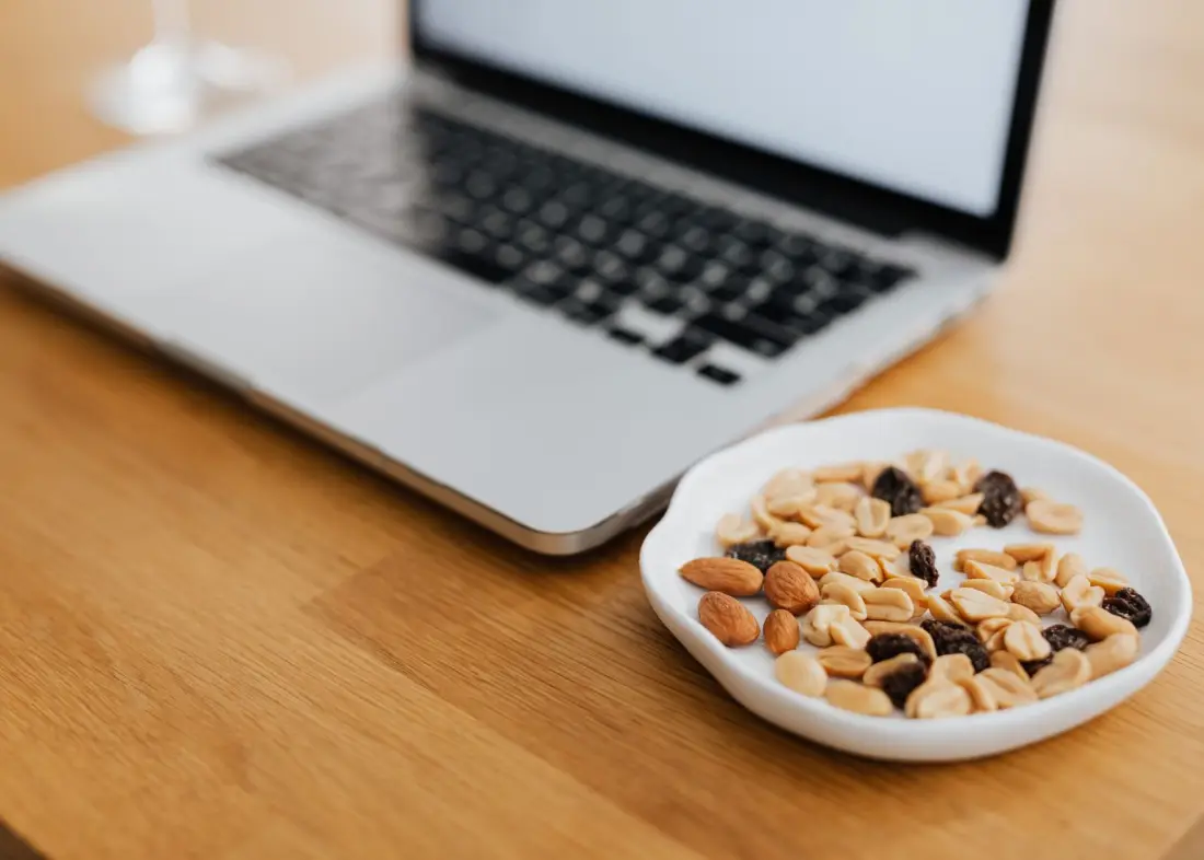 A plate of mixed nuts next to a laptop on a work desk