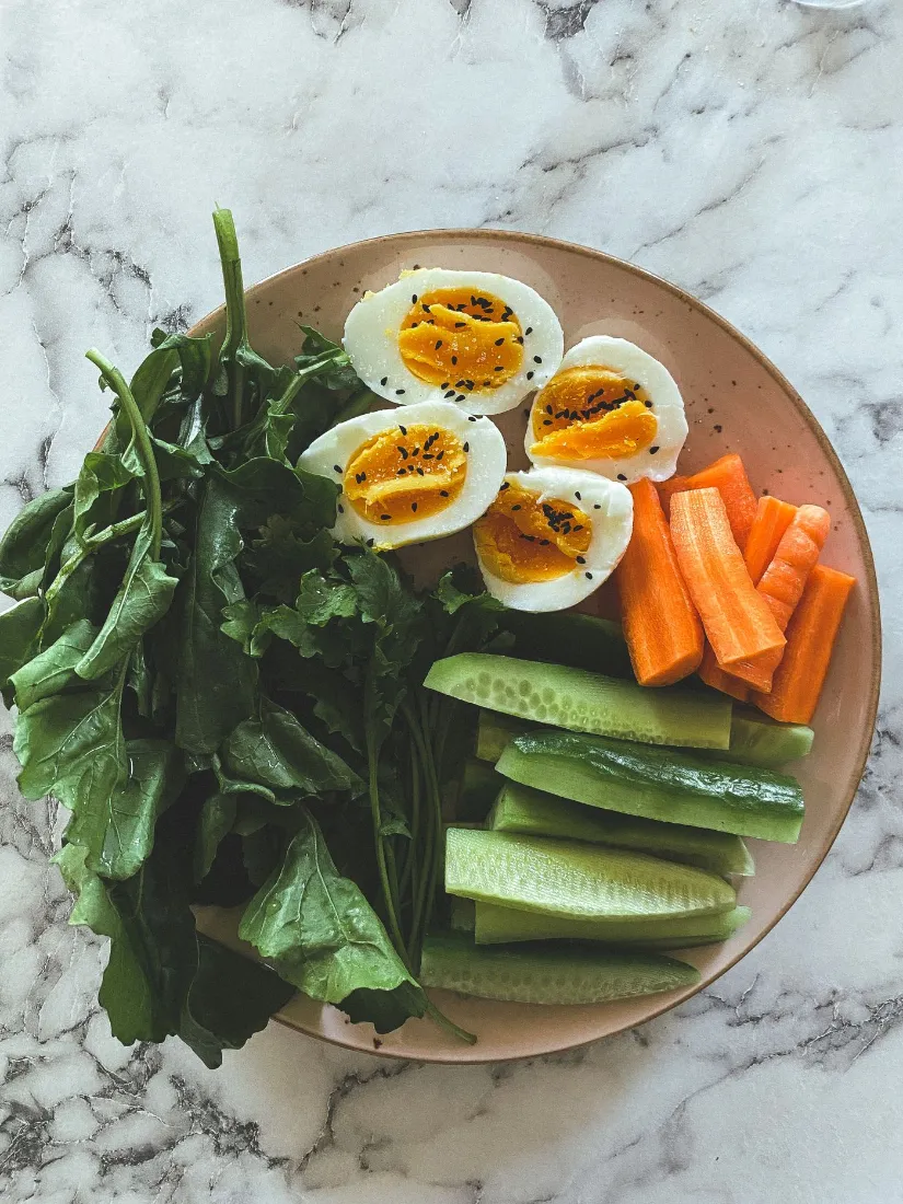 Plate of boiled eggs with spinach, carrot sticks and cucumber, a protein-first breakfast for insulin resistance