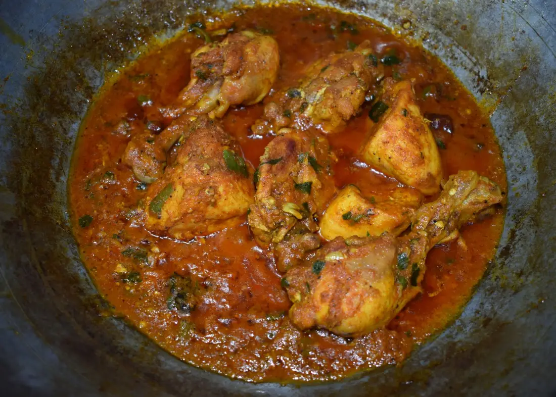 Karahi cooking in an iron wok with oil pooled on top