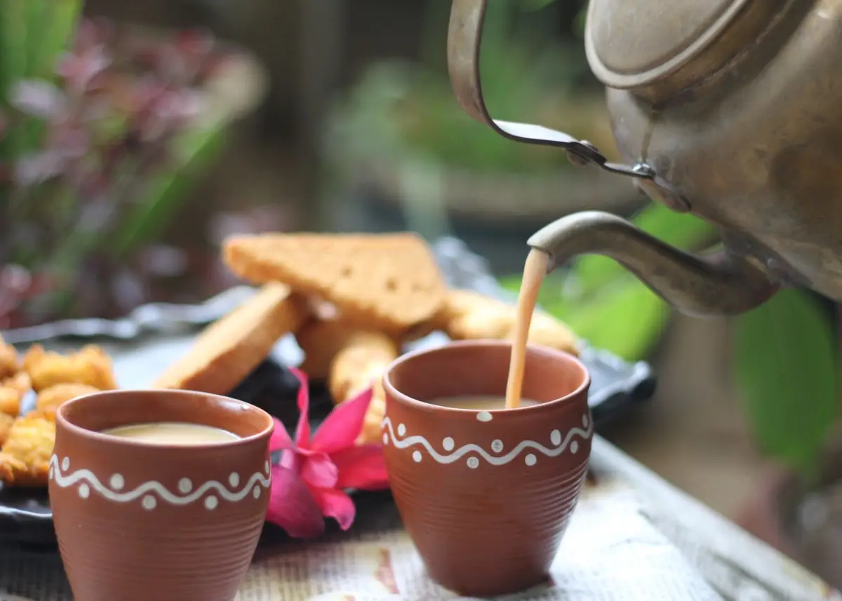 Chai being poured into clay cups with rusks on the side